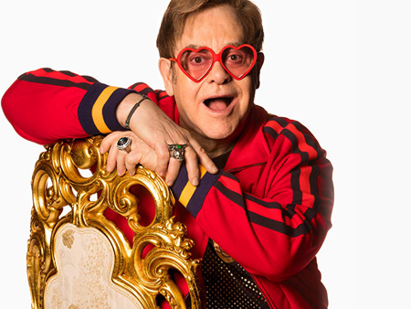 Elton John wears heart glasses and poses for a photo.